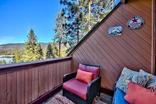 Cozy balcony with colorful cushions, overlooking a scenic lake and pine trees under a clear blue sky.