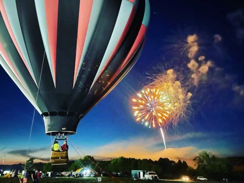 A hot air balloon with a colorful pattern against a night sky, as fireworks burst in the background.