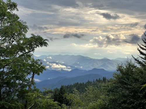 A scenic view of layered mountains under a cloudy sky, with lush greenery in the foreground.