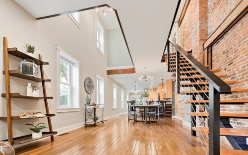 Bright, modern interior featuring a wooden staircase, brick wall, and open dining area with natural light.