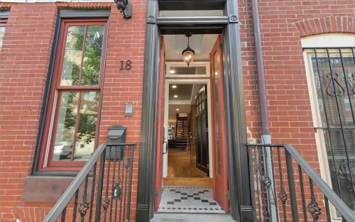 Front entrance of a brick building with a decorative door, steps, and a welcoming interior visible through the doorway.