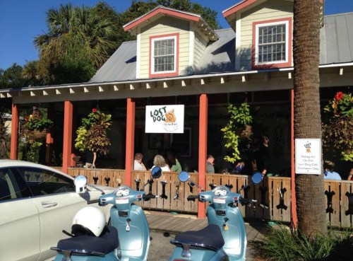 A colorful restaurant with a sign reading "Lost Dog Cafe," featuring outdoor seating and vintage scooters parked nearby.