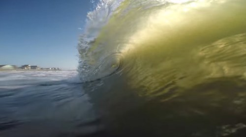 A close-up view of a wave curling in the ocean, with sunlight reflecting off the water's surface.