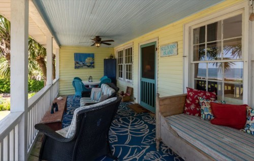 Cozy porch with colorful seating, a ceiling fan, and ocean views, surrounded by palm trees and a welcoming atmosphere.