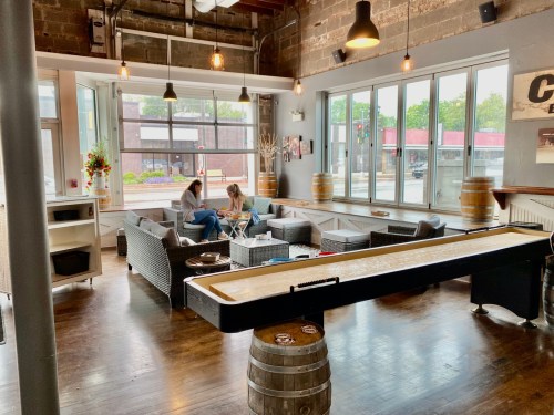 A cozy café interior with large windows, featuring two people sitting at a table and a shuffleboard table in the foreground.