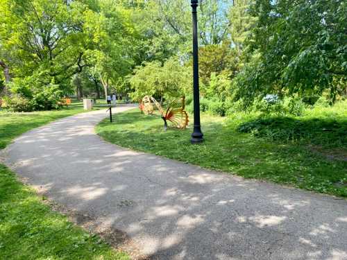 A winding path in a green park with a large butterfly sculpture beside it, surrounded by trees and foliage.