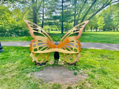 A large, decorative butterfly sculpture in a green park, surrounded by trees and grass.