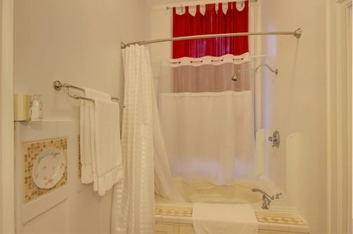 A bright bathroom featuring a bathtub with a shower curtain, red accents, and neatly arranged towels.