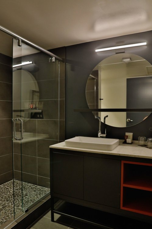 Modern bathroom featuring a glass shower, circular mirror, and sleek vanity with a stone countertop.