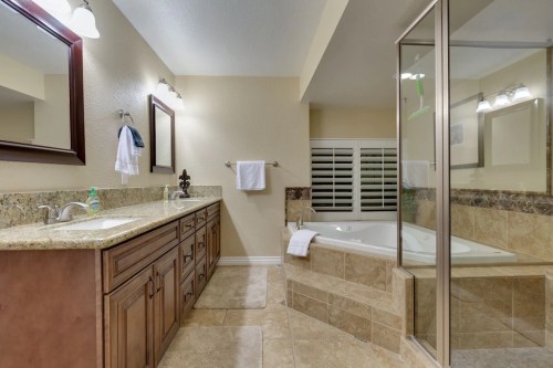 Spacious bathroom featuring a double vanity, glass shower, and a jetted tub with stone accents and neutral tones.