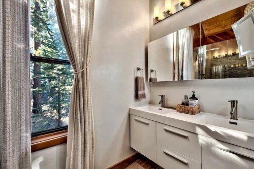 Modern bathroom with a sleek vanity, large mirror, and natural light from a window overlooking trees.