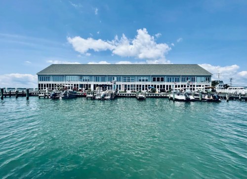 A waterfront building with large windows, surrounded by boats docked in clear blue water under a sunny sky.