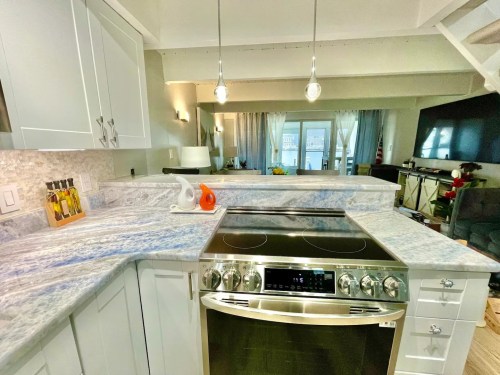 Modern kitchen with marble countertops, stainless steel stove, and bright natural light from large windows.
