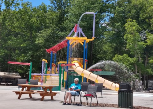 A colorful water play area with a slide and water features, with a person sitting nearby on a bench.