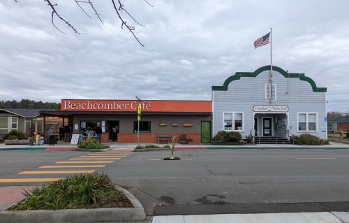 A street view featuring Beachcomber Café with an orange awning and a historic building with an American flag.