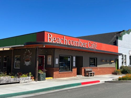 Exterior of Beachcomber Café with a colorful sign, surrounded by flowers and a clear blue sky.