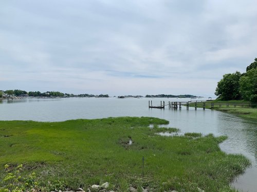 A serene view of a calm waterway with green grass and a wooden dock under a cloudy sky.