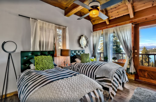 Cozy bedroom with two twin beds, green accents, wooden ceiling, and large windows showcasing a scenic view.