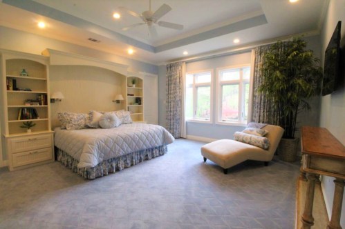 Spacious bedroom with a large bed, chaise lounge, built-in shelves, and large windows letting in natural light.
