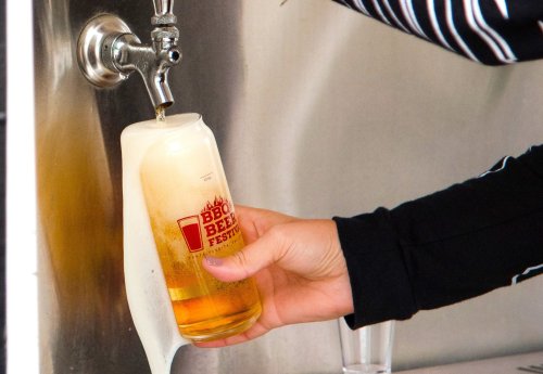 A hand pours beer from a tap into a glass, with foam overflowing from the top.