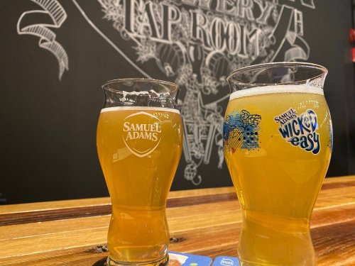 Two glasses of beer on a wooden table, with a chalkboard backdrop featuring "Brewery Tap Room" design.