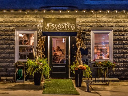 A cozy restaurant entrance with a sign reading "Blacksmith," surrounded by plants and autumn decorations.