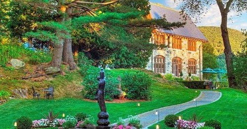A charming stone house surrounded by lush greenery and a well-maintained garden with a pathway and decorative lights.