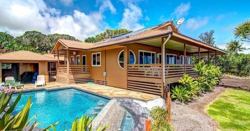 A charming wooden house with a pool, surrounded by lush greenery and blue skies.