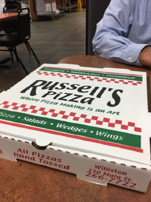 A pizza box from Russell's Pizza, featuring the slogan "Where Pizza Making Is an Art," on a table in a restaurant.