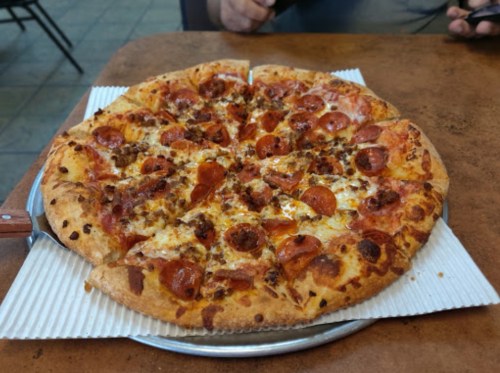 A freshly baked pizza topped with pepperoni and sausage, served on a white paper plate.