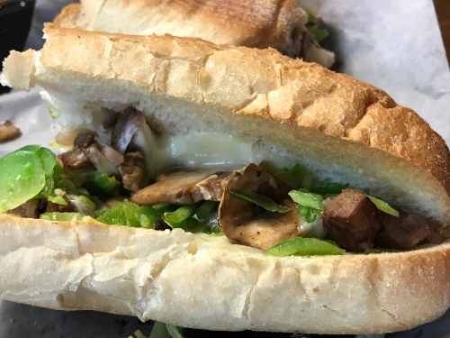 Close-up of a sandwich filled with mushrooms, lettuce, and melted cheese, served on a toasted hoagie roll.