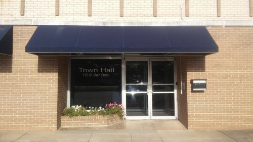 Exterior of a Town Hall building with a blue awning, glass doors, and a flower planter at the entrance.