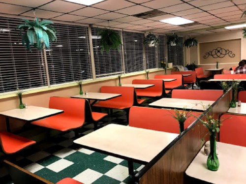 A retro diner interior with orange booths, green checkered floor, and small vases of flowers on tables.