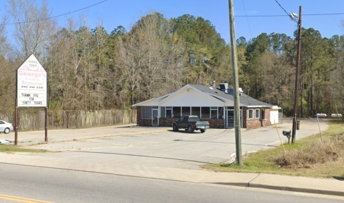 A brick restaurant with a sign reading "George's" and a parking lot, surrounded by trees.