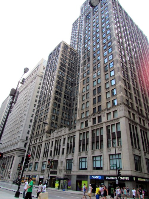 Tall buildings with a mix of modern and classic architecture, bustling street with pedestrians and storefronts below.