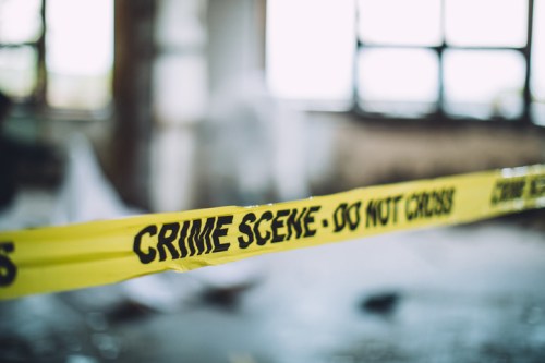 Yellow crime scene tape in an abandoned building, with blurred background and natural light coming through windows.
