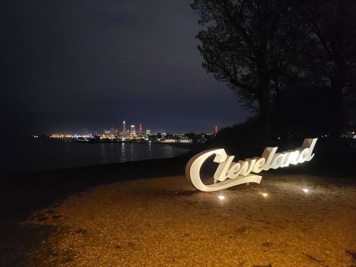 Cleveland sign illuminated at night with city skyline and water in the background.