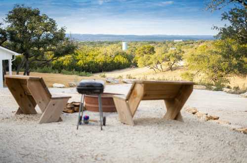 A scenic outdoor view with two wooden benches facing a distant landscape and a grill on gravel ground.