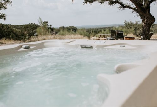 A hot tub with bubbling water, set in a scenic outdoor landscape with trees and distant hills.