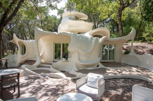 A unique, sculptural white house surrounded by trees, featuring organic shapes and large windows.