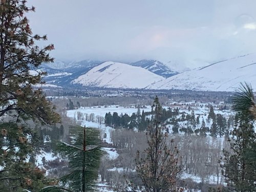 Snow-covered mountains and a valley with trees, under a cloudy sky, creating a serene winter landscape.