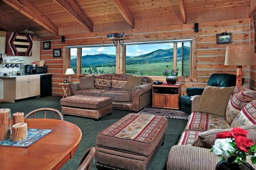 Cozy cabin interior with wooden walls, a sofa, and a scenic view of mountains through large windows.
