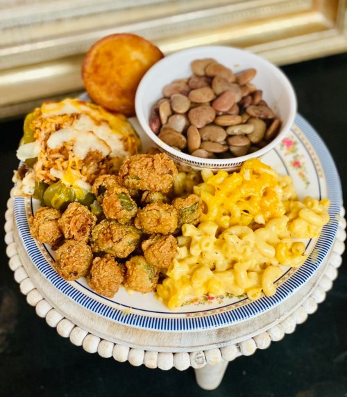 A plate of Southern comfort food featuring fried okra, macaroni and cheese, cornbread, and a bowl of mixed beans.