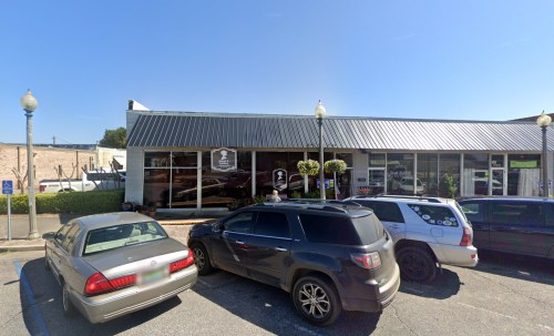 A storefront with a metal roof, surrounded by parked cars and street lamps under a clear blue sky.