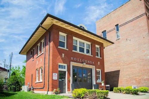 Historic red brick firehouse with large windows and a sign reading "Hose Co. No. 4," set against a blue sky.
