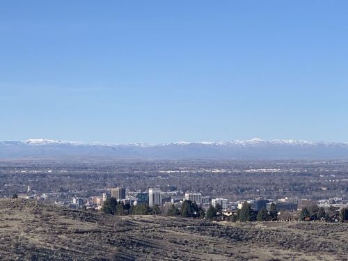 A panoramic view of a city skyline with mountains in the background under a clear blue sky.