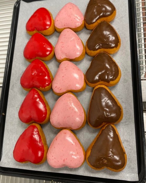 A tray of heart-shaped donuts with red, pink, and chocolate icing arranged in rows.