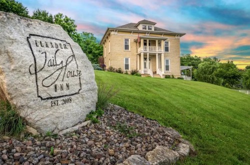 Historic Jail House Inn with a stone sign, set against a colorful sunset and lush green landscape.