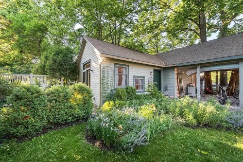 A charming house surrounded by lush greenery and a colorful garden, with a garage visible on the side.