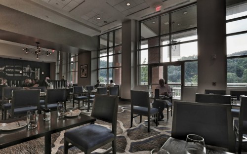 A modern restaurant interior with large windows, tables set for dining, and a few patrons enjoying their meals.